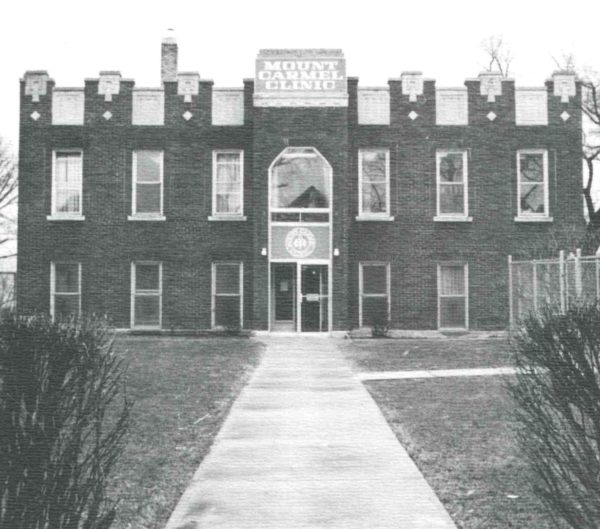 A grainy black and white photo shows a brick building that says Mount Carmel Clinic on it.