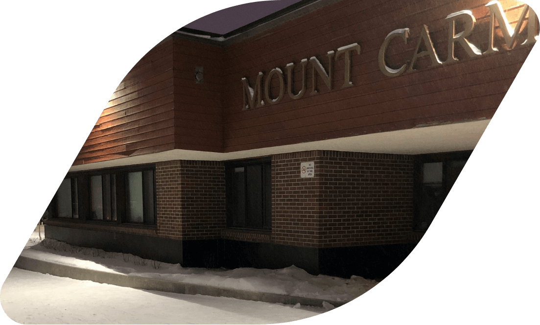 The exterior entrance of Mount Carmel Clinic. The building is brown brick and painted brown wood.